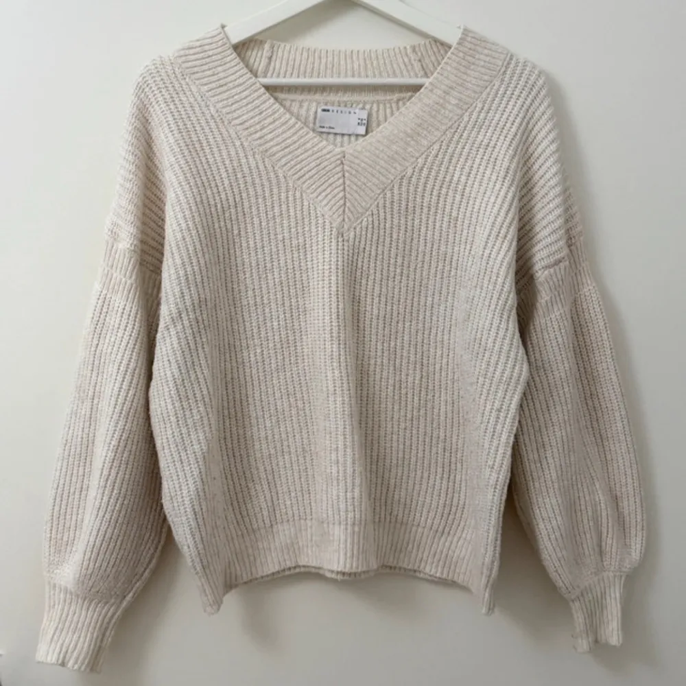 Säljer en beige stickad tröja från ASOS DESIGN med bred v-ringning och lång ärm. Tröjan har en avslappnad passform och är gjord i en mjuk blandning av polyester och akryl. . Neuletakit & Villapaidat.