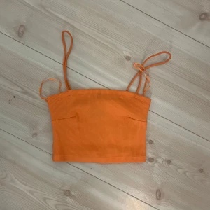 Orange ribbad croppad linnetopp från Gina  - Säljer en orange ribbad croppad linnetopp med smala axelband och knyt på ena axeln. Perfekt för varma dagar och enkel att matcha med jeans eller kjol.