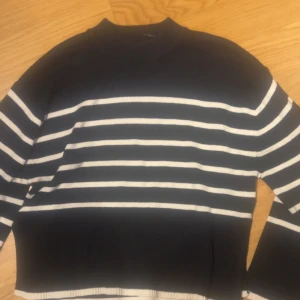 Svart och vit randig stickad tröja från Gina Tricot - Säljer en svart stickad tröja från Gina Tricot i storlek XS. Tröjan har vita horisontella ränder och ribbade muddar vid hals, ärmslut och nederkant. Perfekt för en stilren och avslappnad look.