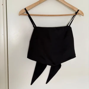 Svart croppad linnetopp från Renuar - Säljer en svart croppad linnetopp från Renuar med smala justerbara axelband och knytband baktill. Toppen har en slät framsida och smockad rygg för extra komfort. Perfekt till sommaren!
