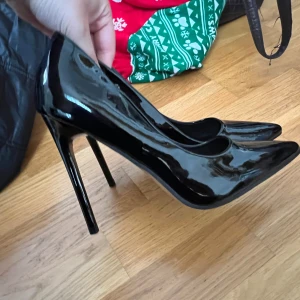 Svarta lackpumps med spetsig tå och hög klack - Säljer ett par glansiga svarta pumps med spetsig tå och riktigt hög klack. Skorna har en elegant och klassisk design som passar perfekt när du vill sticka ut lite extra.