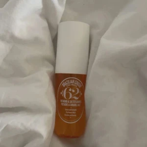 Brazilian Crush Cheirosa '62 Parfymmist - En ikonisk parfymmist från Sol de Janeiro med doft av pistage och salt karamell. Flaskan är genomskinlig med orange ton och har ett vitt, cylinderformat lock. Perfekt för dig som älskar söta och varma dofter.