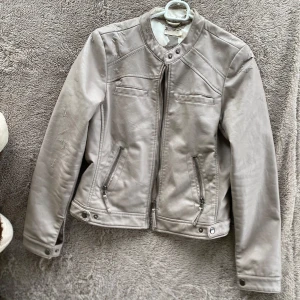 Ljusgrå/ beige skinnjacka - Säljer en ljusgrå skinnjacka med snygga detaljer och dragkedjor framtill. Jackan har defekter! kolla sista bilden!!!