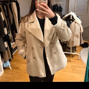 Beige skepparkavaj med dubbelknäppning - Säljer en stilren beige skepparkavaj med bred krage och dubbelknäppning framtill. Jackan har långa ärmar och två fickor på sidorna. Perfekt för dig som vill ha en klassisk look.