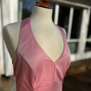 Aftonklänning med v-ringning - Säljer en elegant rosa långklänning med djup v-ringning och breda axelband. Klänningen har en figurnära överdel och utsvängd kjol med fina sömdetaljer. Perfekt för bal eller festliga tillfällen.