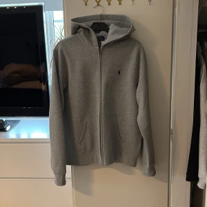 Ralph lauren hoodie  - Säljer en grå hoodie från Polo Ralph Lauren med dragkedja och huva. Tröjan har två fickor framtill och broderad logga på bröstet. Knappt använd, max 2-3 gånger. Ser ut och känns som ny. Storlek XL(18-20)