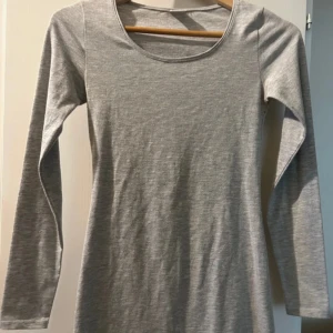 Grå långärmad klänning från Gina Tricot - Säljer en enkel och stilren grå långärmad klänning från Gina Tricot i storlek XS. Klänningen har rund halsringning och är tillverkad i mjukt bomullsmaterial. Klänningen slutar lite ovanför knärna.
