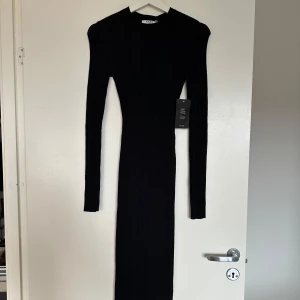Svart ribbad långklänning från NA-KD - Säljer en svart ribbad långklänning från NA-KD med lång ärm och en snygg öppen rygg. Klänningen har en tight passform och är perfekt för dig som vill ha en stilren och trendig look.