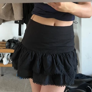 Svart volangkjol - Säljer en svart kortkjol med volanger. Kjolen har en midja och flera lager volang som ger en snygg och lekfull look. Perfekt att styla med en enkel topp eller hoodie.