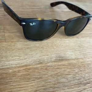 Ray-Ban Wayfarer solglasögon - Klassiska Ray-Ban Wayfarer solglasögon med brunmelerat skal och svarta glas. Snygg och tidlös design med Ray-Ban-logga på bågen. Kommer med originalfodral. Inga repor, välskötta, Pris kan diskuteras, Ny pris 1100kr