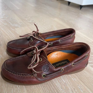 Timberland seglarskor i läder – ca storlek 35,5 - Säljer ett par klassiska seglarskor från Timberland i brunt läder. Skorna är i relativt gott skick och nyligen inoljade/inrättade, vilket gör att de är mjuka och bekväma att använda direkt. Passar fot som är cirka 22,3 cm lång – ungefär storlek 35,5. Skorna är perfekta till både vår och sommar, snygga till både vardags- och lite mer uppklädda tillfällen. Nypris för liknande Timberland-skor ligger runt 1000–1300 kr. Hör av dig om du vill ha fler bilder eller har någr frågor!