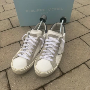 Vita sneakers från Philippe Model - Snygga vita sneakers från Philippe Model med gråa och mörkblåa detaljer. Skorna har en klassisk design med snörning och rund tå. Perfekta för en stilren look. Org pris runt 3-4 tusen kr