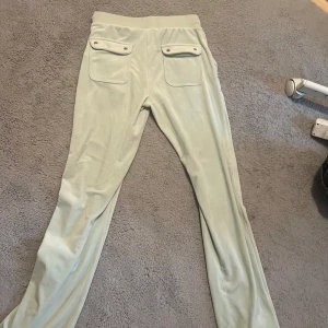Ljusgrönt set från Juicy Couture - Säljer ett par ljusgröna velourbyxor från Juicy Couture med raka ben och två fickor med knappar bak. Byxorna har en mjuk och stretchig känsla, perfekta för en avslappnad stil. Byxorna är helt nya köpta för 1200 har bara prövat en gång, dem var för små för mig.