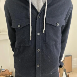 J.lindberg overshirt - Säljer en mörkblå overshirt med knäppning framtill och två bröstfickor med lock och knappar. Jackan har lång ärm och en avslappnad passform, perfekt att slänga över en hoodie.