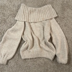 Beige stickad offshouldertröja från Gina Tricot - Supermysig beige stickad tröja från Gina Tricot med bred offshoulderkrage och långa ärmar. Perfekt för kyligare sommar dagar och enkel att styla med jeans eller kjol. Ribbstickade muddar vid ärmslut och nederkant.