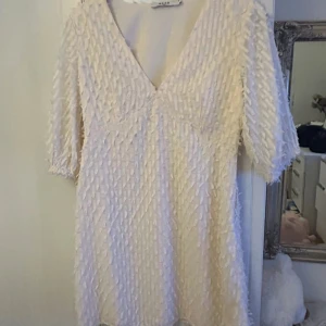 Vit kortklänning med struktur från NA-KD - Säljer en vit kortklänning från NA-KD med v-ringning och trekvartsärm. Klänningen har ett unikt strukturerat tyg med små tygdetaljer över hela ytan. Perfekt för dig som vill sticka ut med en stilren och modern look. Vit/beige