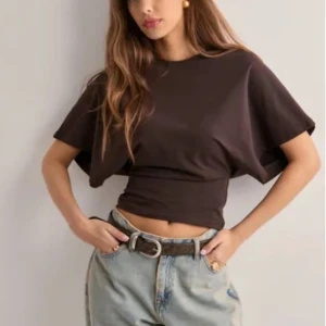 Brun Topp - Säljer en brun croppad t-shirt med korta ärmar och rund halsringning. Toppen har en tight passform vid midjan och är tillverkad i ett mjukt bomullsmaterial. Perfekt att matcha med jeans eller kjol. Använt fåtal gånger!
