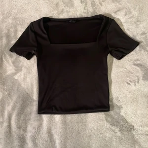 Svart topp med fyrkantig ringning - Säljer en svart topp med korta ärmar och snygg fyrkantig ringning. Toppens material är stretchigt och sitter tight mot kroppen, perfekt att styla till olika outfits.