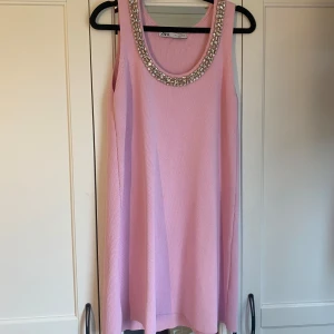 Ljusrosa ärmlös klänning med detaljer från Zara - Supersöt ljusrosa ärmlös klänning från Zara med rund halsringning dekorerad med stenar. Klänningen har en rak, lös passform och är tillverkad i ett ribbat material.