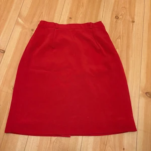 Röd kjol - Säljer en klassisk röd kjol med rak passform och enkel design. Kjolen har resår och dragkedja bak för en bekväm passform. Perfekt att styla med en enkel topp eller stickad tröja. Sömmen har gått upp lite i slitsen men inget som påverkar funktionen. En liten fettfläck som jag inte testat tvätta bort. 