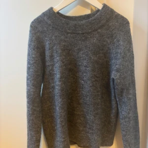 Grå stickad tröja från Saint Tropez - Mysig grå stickad tröja från Saint Tropez med bred ribbad krage. Tröjan har lång ärm och är perfekt för kyligare dagar. Enkel och stilren design som passar till många olika outfits.