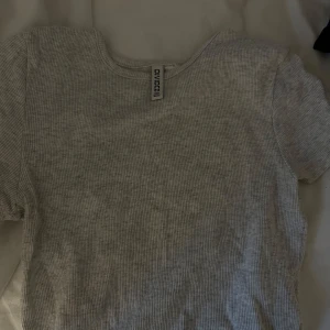 Ljusgrå ribbad topp från H&M Divided - En ljusgrå ribbad topp från H&M Divided med rund halsringning och korta ärmar. Perfekt basplagg i mjuk bomullsblandning som passar till många olika outfits.