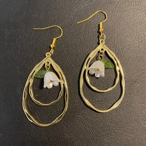 Guldiga örhängen med blomdetalj - Unika örhängen i guldmetall med två vågiga droppformade ringar och en vit blomma med grön blad-detalj i mitten. Perfekta för vår och sommar tider! (Självgjorda örhängen)