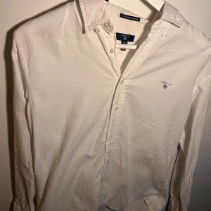 Vit skjorta från Gant - Klassisk vit skjorta från Gant med broderad logga på bröstet och knappar framtill. Skjortan har lång ärm och button-down krage, perfekt för en clean och stilren look.