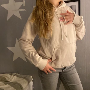 Beige hoodie från H&M - Säljer en beige hoodie i storlek XS med klassisk känguruficka och huva med dragsko. Tröjan har långa ärmar och är tillverkad i mjukt bomullsmaterial. Perfekt för en avslappnad och stilren look.