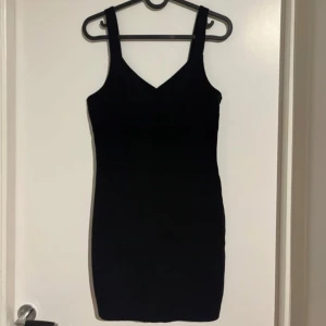 Svart tight klänning med v-ringning - Säljer en svart tight klänning med breda axelband och v-ringad hals. Klänningen är kort och har en enkel, stilren design som passar perfekt till olika tillfällen. Materialet känns mjukt och följsamt. Väldigt kort på mig (170cm)