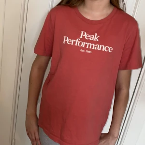 Röd/orange t-shirt från Peak Performance - Säljer en röd/orange t-shirt från Peak Performance med vit logga framtill. T-shirten har rund halsringning och är tillverkad i mjuk bomull. Perfekt basic-plagg med normal passform och korta ärmar.