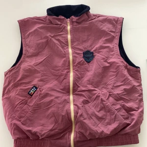 Vinröd väst med dragkedja - Säljer en vinröd väst från Schott med gul dragkedja och ribbade muddar. Väst med två fickor framtill och svart insida. Perfekt för lager-på-lager och har en klassisk look.