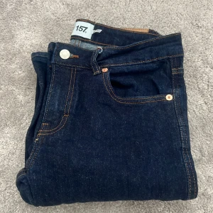 Mörkblå jeansbyxor från 157 - Säljer ett par mörkblå jeansbyxor från 157 med klassisk femficksdesign och kontrastsömmar. Byxorna har raka, vida ben och normal passform. Perfekta för dig som gillar en enkel och stilren look.