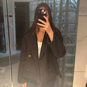 Svart kappa från Stradivarius - Säljer en svart kappa från Stradivarius i storlek XS. Jackan har bred krage, dubbelknäppning med stora knappar och en något oversized passform. Endast använd några få gånger.