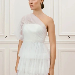 Vit klänning, studentklänning, examens klänning  - Säljer en elegant vit oneshoulder klänning från by Malina med flera lager av tunn, plisserad tyll och volangdetaljer. 