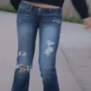 Blå slitna bootcut jeans - Säljer ett par blå bootcut jeans med slitningar och hål på benen. Jeansen har låg midja och klassisk femficksdesign. 