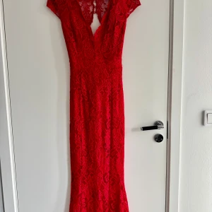 Röd långklänning i spets med v-ringning - Säljer en röd långklänning i spets med v-ringning och korta ärmar. Klänningen har öppen rygg och figurnära passform, perfekt för fest eller bal. Detaljerad spets över hela klänningen ger en elegant look. Jag använde denna på min bal och var extremt nöjd och fick många fina komplimanger. Klänningen har använts en gång och är i fint ny skick.