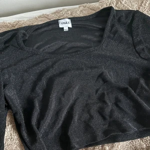 Svart glittrig croppad topp från RAVLS - Säljer en svart glittrig croppad topp från RAVLS. Toppen har lång ärm och en snygg v-ringning. Perfekt för dig som vill sticka ut lite extra med en stilren men ändå festlig look.