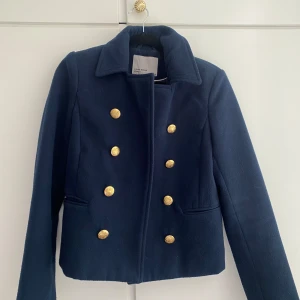 Mörkblå kavajjacka med guldknappar - Säljer en mörkblå kavajjacka från Vero Moda  med dubbelknäppning och dekorativa guldknappar framtill. Jackan har klassisk krage och långa ärmar. Perfekt för en stilren look.