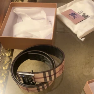 Burberry bälte - Säljer ett klassiskt rutig bälte från Burberry med silverfärgat spänne. Bältet har den ikoniska beige, svarta och röda färgkombinationen och levereras i originalask med dustbag. Perfekt accessoar för att lyfta din outfit.