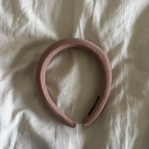 Beige vadderat diadem - Säljer ett beige, vadderat diadem med bred form. Diademet har en mjuk yta i tyg och ger en trendig look till din outfit. Perfekt accessoar för att lyfta din stil.
