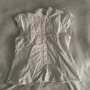 Vit blus med spetsdetaljer från Flash Basic - Säljer en söt vit blus från Flash Basic med korta ärmar och fina spetsdetaljer framtill. Blusen har knappar hela vägen och en liten ståkrage. Skulle nog säga att den passar s/m/L i storlek. Säljer då den aldrig är använd, köpt från vinted!