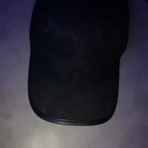 Svart keps med justerbart spänne - Säljer en stilren svart keps med böjd skärm och justerbart metallspänne baktill. Perfekt för dig som vill ha en enkel och klassisk look. Passar till många olika outfits. Intresserad av byta mot gamla modellen Gucci keps i svart storlek M