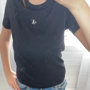 Svart t-shirt från Calvin Klein Jeans - Svart t-shirt från Calvin Klein Jeans med liten vit CK-logga på bröstet. Klassisk rund halsringning och korta ärmar. Perfekt basplagg i mjuk bomull som passar till det mesta.