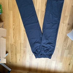 Mörkgrå/blå byxor med resår i midjan - Säljer ett par mörkgrå byxor med resår i midjan och raka/vida långa ben. Byxorna har fickor i sidorna och en dekorativ bakficka. Perfekta för en avslappnad men stilren look. Använda en gång!