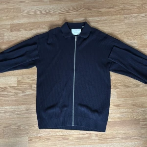 Mörkblå stickad jacka med dragkedja från Jack & Jones - Säljer en mörkblå stickad jacka från Jack & Jones med hel dragkedja framtill och klassisk krage. Jackan har lång ärm och en stilren, enkel design som passar perfekt till vardags. Materialet är mjukt och bekvämt.