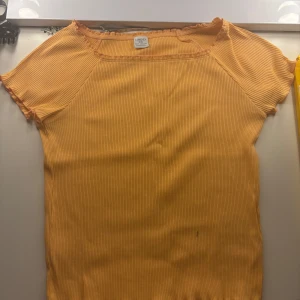 Gul ribbad topp från Lindex Kids - Säljer en söt gul ribbad topp från Lindex Kids i storlek 146/152. Toppen har korta ärmar, rund halsringning och vågiga kanter vid hals och ärmslut. Perfekt för dig som gillar färgglada och bekväma plagg!