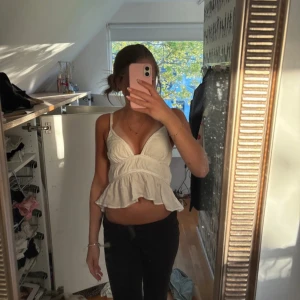 Vit volangtopp från Zara - Säljer en söt vit topp från Zara med volang och smala axelband. Toppen är croppad och har knytning i ryggen.