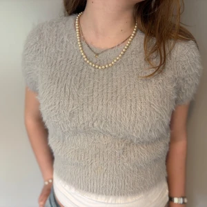 Ljusgrå fluffig tröja från Zara - Supermjuk och fluffig ljusgrå tröja från Zara med korta ärmar och rund hals. Tröjan har en croppad passform och är perfekt för dig som gillar en mysig och trendig stil. Passar snyggt till både jeans och kjol.