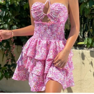 Rosa klänning - Supersöt kort klänning i rosa med blommigt mönster och volanger. Aldrig använd och i superfint skick. Perfekt för sommarens alla tillfällen!